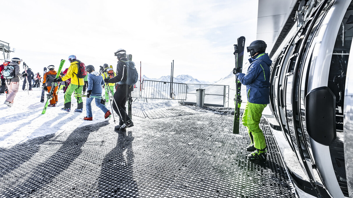 Wintersportler steigen mit Ski und Snowboard in die moderne Gondelbahn in St. Anton ein.