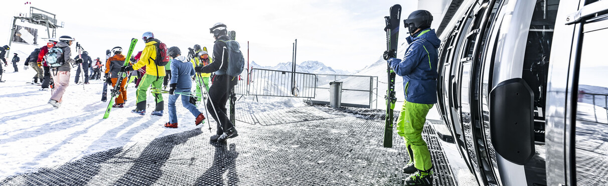 Skiers and snowboarders board a modern gondola lift in St. Anton am Arlberg.
