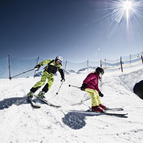 Father skiing with daughter on a secure slope under the bright sun in the Arlberg ski area.