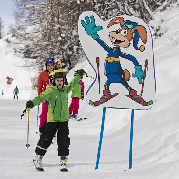 Child skis through the playful Hopplweg and raises his hand to shake hands with a cartoon character of a rabbit.