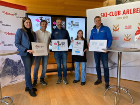 Fünf Personen präsentieren das Logo der FIS Alpinen Junioren Ski-Weltmeisterschaft 2023 in St. Anton am Arlberg. Im Hintergrund ein Bildschirm mit dem Veranstaltungslogo.