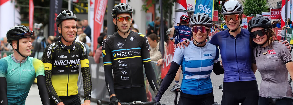 Teilnehmerinnen und Teilnehmer des Arlberg Giro posieren lächelnd in Fahrradkleidung vor dem Startbereich.