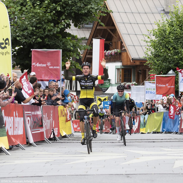 Ein Radfahrer überquert jubelnd die Ziellinie beim Arlberg Giro, dicht gefolgt von weiteren Fahrern.