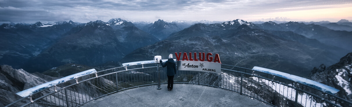 Person steht an der Plattform Valluga in St. Anton und blickt auf ein weites Panorama mit dunklen Bergketten.