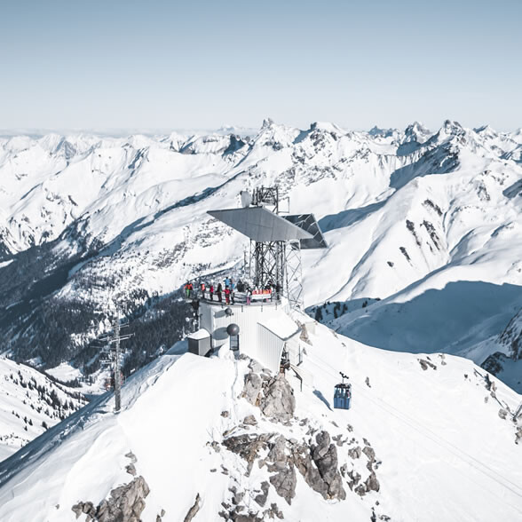 Viewing platform on Valluga with visitors and panoramic view over the snowy Arlberg mountains.