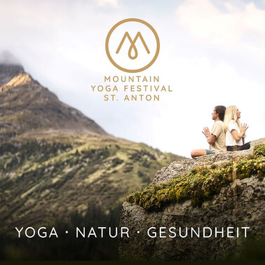 Two people sit back to back at the yoga festival in green alpine surroundings.