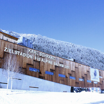 Das Karl-Schranz-Zielstadion der Ski-WM 2001 mit Holzfassade und großem Schriftzug. Im Hintergrund ein verschneiter Berghang.