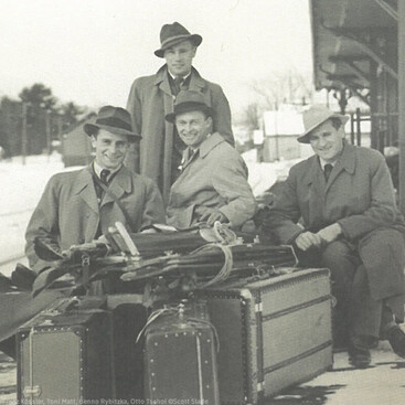 Franz Kössler, Toni Matt, Benno Rybitzka, Otto Tschol sitzen auf Gepäck an einem Bahngleis