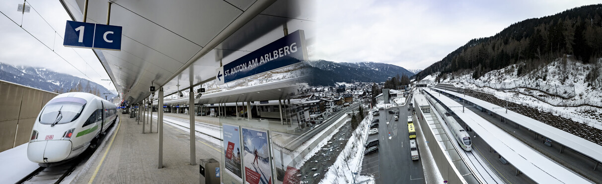 Ein moderner ICE-Zug der Deutschen Bahn steht am schneebedeckten Bahnhof St. Anton am Arlberg. Im Hintergrund sind winterliche Berge und ein Teil der Ortschaft zu sehen. Die Gleise und das Bahnsteigdach sind teilweise mit Schnee bedeckt.