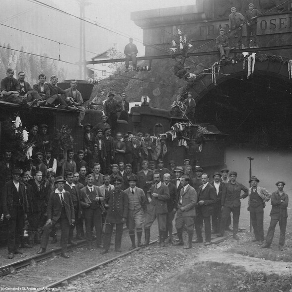 Schwarz-Weiß-Foto zeigt Arbeiter und Einheimische bei einer feierlichen Eröffnung vor einem Bahntunnel.