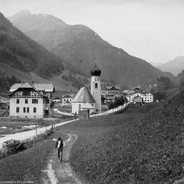 Historische Aufnahme eines alpinen Dorfs mit markanter Kirche mit Zwiebelturm, umgeben von Bergen.