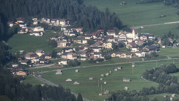 Luftaufnahme von Schnann mit Kirche, umgeben von grünen Wiesen und Wäldern.