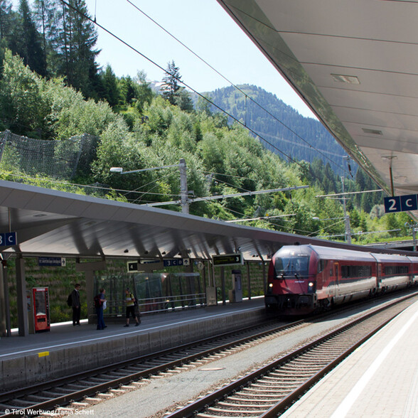 Roter ÖBB-Zug hält am Bahnsteig inmitten einer bewaldeten Berglandschaft in St. Anton am Arlberg.
