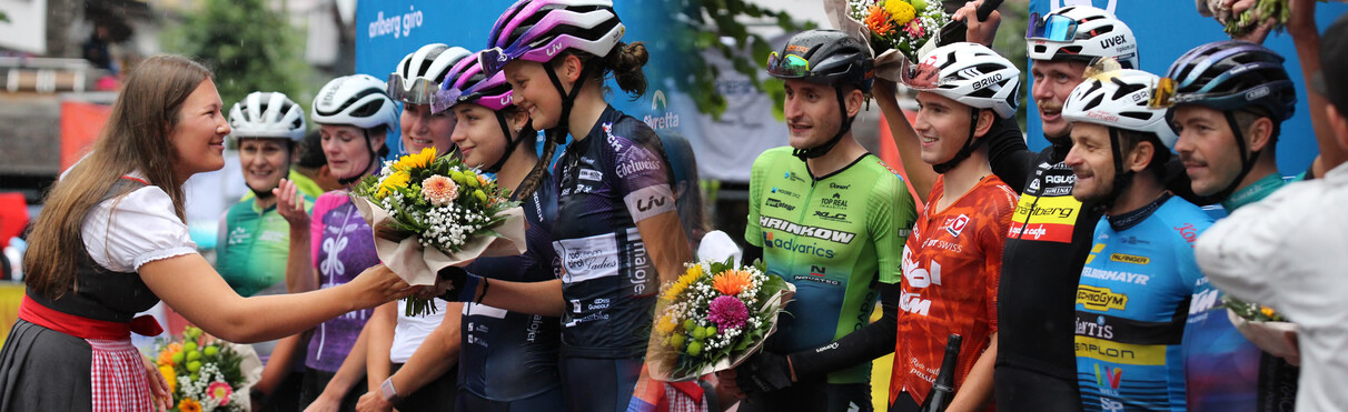 Teilnehmer:innen des Radrennens erhalten bei der Siegerehrung Blumensträuße von einer Frau in Tracht.