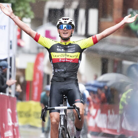Ein männlicher Radfahrer im Trikot des Teams Vorarlberg jubelt mit ausgebreiteten Armen im Zielbereich.