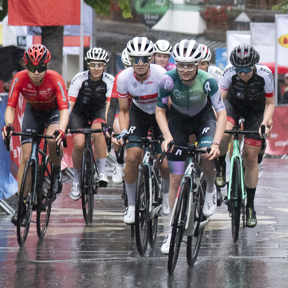 Eine Gruppe weiblicher Rennradfahrerinnen fährt gemeinsam im Regen auf nasser Straße, konzentriert und motiviert.