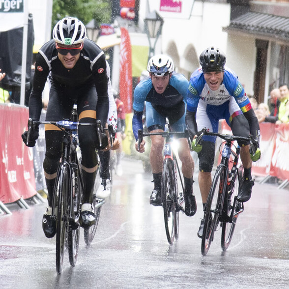 Drei männliche Rennradfahrer im Zielsprint bei starkem Regen in der Fußgängerzone von St. Anton.