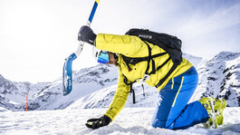 Bergretter in gelber Kleidung bei der Lawinensuche mit Sonde auf verschneitem Hochplateau.
