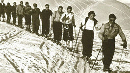 Historisches Foto: Gruppe Skifahrer in Retro-Bekleidung steigt nebeneinander durch tiefen Schnee.