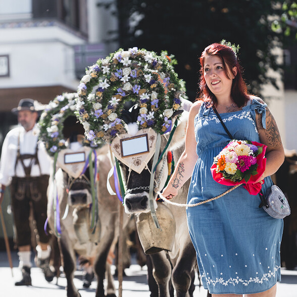 Eine Frau in Tracht führt geschmückte Kühe mit bunten Blumenkränzen durch St. Anton – ein farbenfrohes Highlight des Almabtriebs.