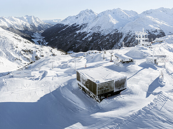 Blick auf das verschneite Skigebiet in St. Anton am Arlberg mit moderner Liftstation im Vordergrund. Im Hintergrund öffnet sich ein tiefes Tal zwischen schneebedeckten Alpen.