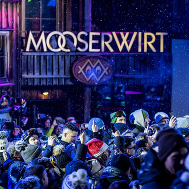 Mooserwirt Terrasse bei Nacht mit Partybeleuchtung und feiernder Menschenmasse in Skiausrüstung.