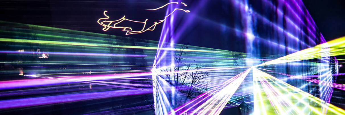 Colorful laser beams in violet, green, and blue pierce the night sky above St. Anton am Arlberg. A spectacular light show with projections like a leaping deer captivates the audience during a wintry evening atmosphere.