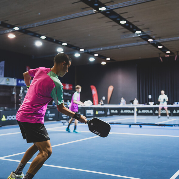 Zwei Spieler beim intensiven Herren-Doppel-Match auf einem blauen Pickleball-Feld. Die Atmosphäre ist energiegeladen.