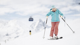 Ältere Frau fährt entspannt Ski, im Hintergrund schwebt die Valluga-Seilbahn.
