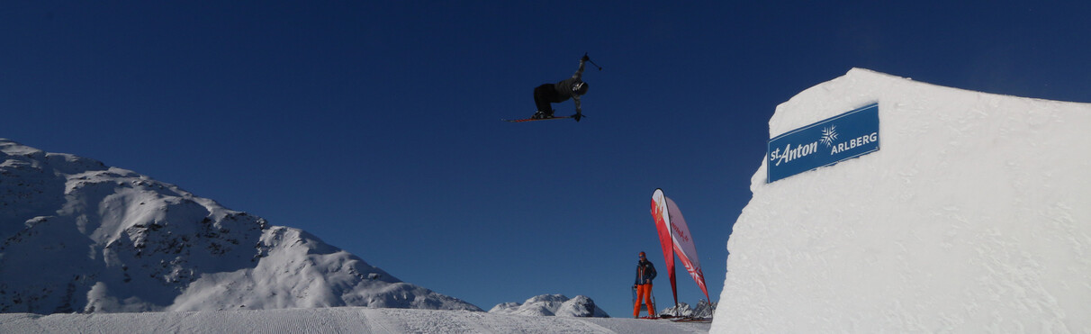 Wintersportler beim FIS Freestyle European Cup in St. Anton mit spektakulärem Sprung vor alpiner Winterlandschaft.
