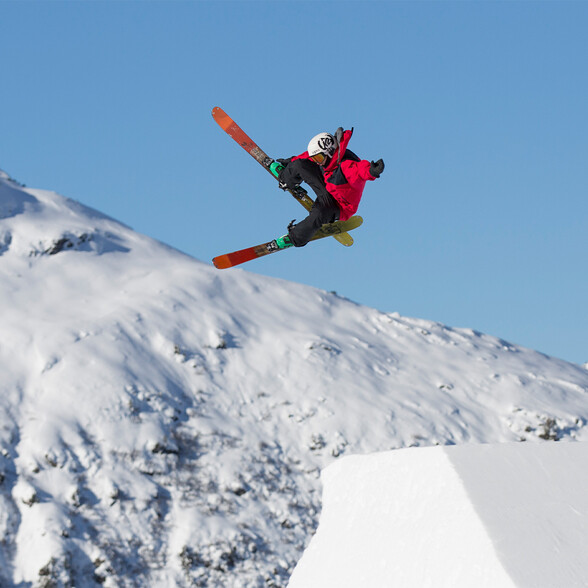 Freestyle-Skifahrer in der Luft bei einem Big-Air-Sprung im Skigebiet St. Anton. Imposante Höhe vor verschneiter Bergkulisse.