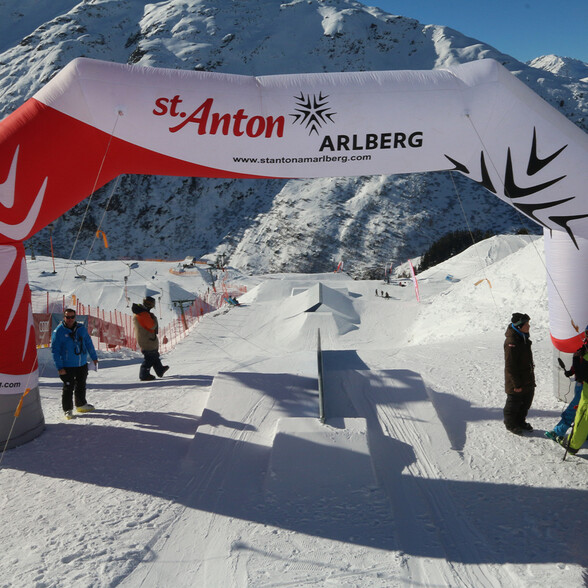 Skigelände in St. Anton am Arlberg mit professionellen Slopestyle-Hindernissen unter strahlend blauem Himmel. Ideal für Freestyle-Wettkämpfe und Wintersportfans.