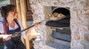 Frau schiebt frische Brote mit Holzschieber in einen Steinofen / Woman placing fresh bread into a stone oven using a wooden peel