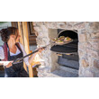 Frau schiebt frische Brote mit Holzschieber in einen Steinofen / Woman placing fresh bread into a stone oven using a wooden peel