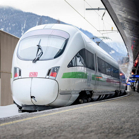 Nahaufnahme eines ICE-Zugs mit grüner Umweltlinie im verschneiten Bahnhof St. Anton. Ein Symbol für nachhaltige Mobilität in den Alpen.