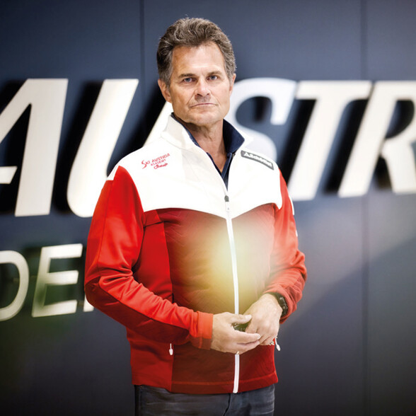 Herbert Mandl, sportlich gekleidet im offiziellen Ski Austria Outfit, posiert vor einer modernen Wandgestaltung. Die Aufnahme zeigt seine enge Verbindung zum Wintersport.