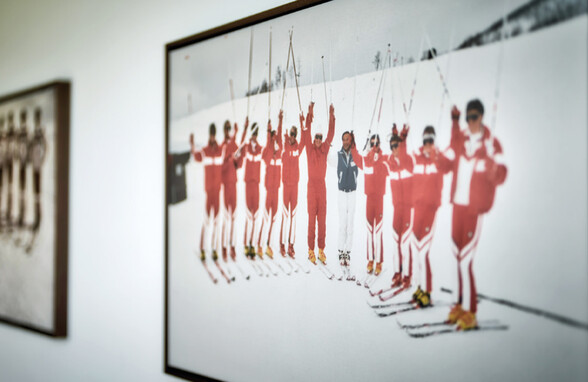 Innenaufnahme aus dem Skimuseum in St. Anton mit historischen Fotos von Skilehrern in roten Anzügen. Die Ausstellung zeigt die Entwicklung des Skisports in der Region.