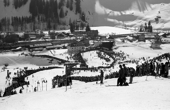 Schwarzweißfoto eines gut besuchten Skirennens in St. Anton am Arlberg. Tausende Zuschauer säumen die Rennstrecke bei einem historischen Wintersportereignis.