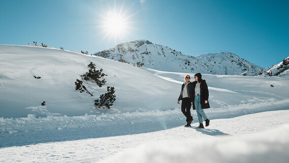 Zwei Menschen spazieren bei Sonnenschein auf einem geräumten Winterwanderweg.