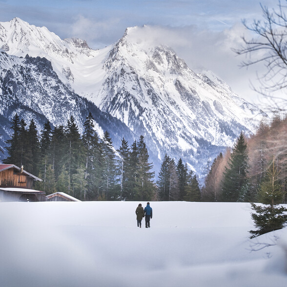 Zwei Menschen wandern auf einem schneebedeckten Weg durch die ruhige Winterlandschaft von St. Anton mit beeindruckendem Bergpanorama.