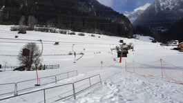 Kleiner Schlepplift mit sanftem Hang und Blick auf verschneite Stadl im Hintergrund.