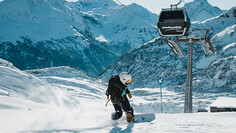 Snowboarder rides through powder snow below Schindlergratbahn with mountain backdrop.