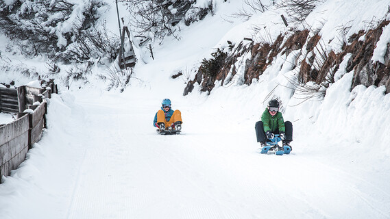 Zwei Kinder rodeln auf der verschneiten Rodelbahn in St. Anton am Arlberg
