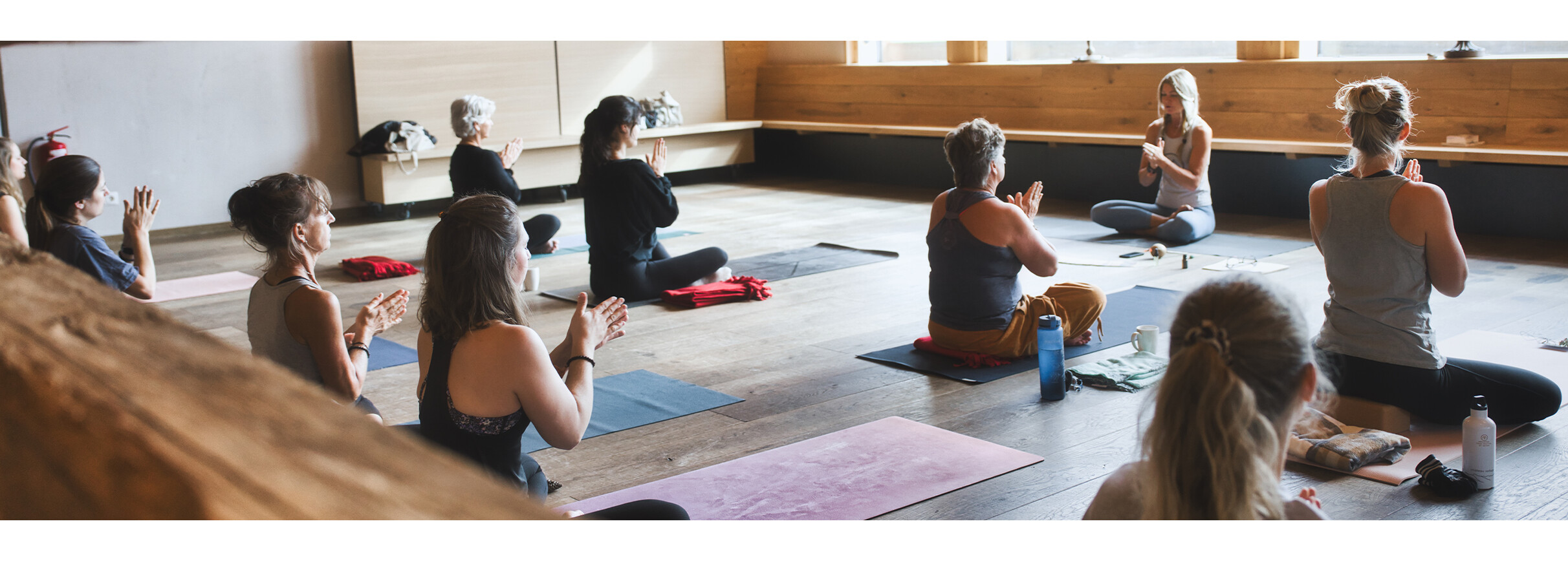 Yoga in St. Anton am Arlberg Mehrere Personen sitzen auf Yogamatten in einem Holzstudio und meditieren gemeinsam im Schneidersitz.