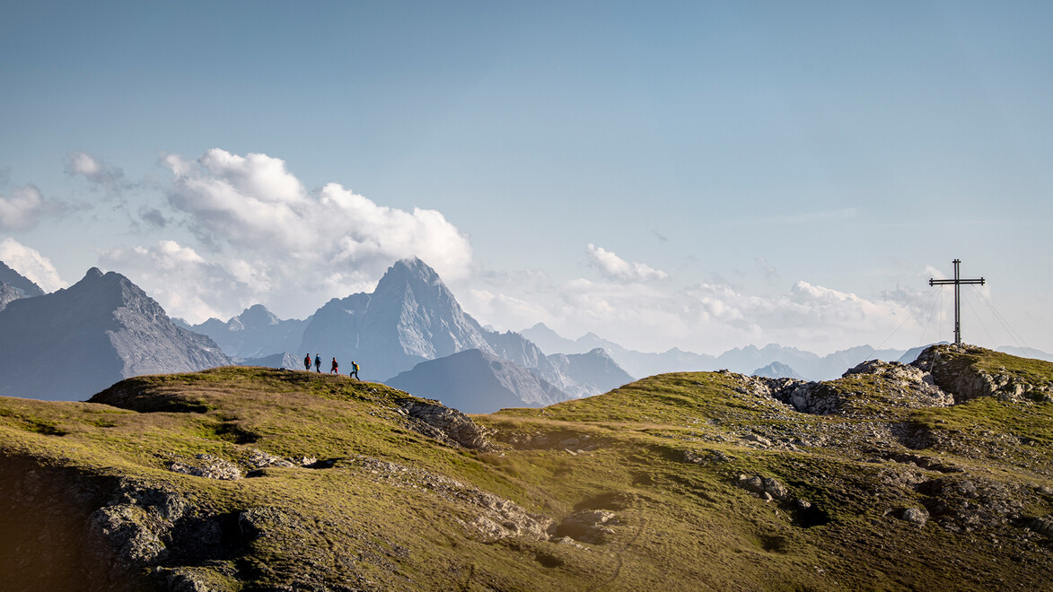 Berggipfel mit Gipfelkreuz und Blick auf markante alpine Berglandschaft / Mountain peak with summit cross and view of distinctive alpine landscape