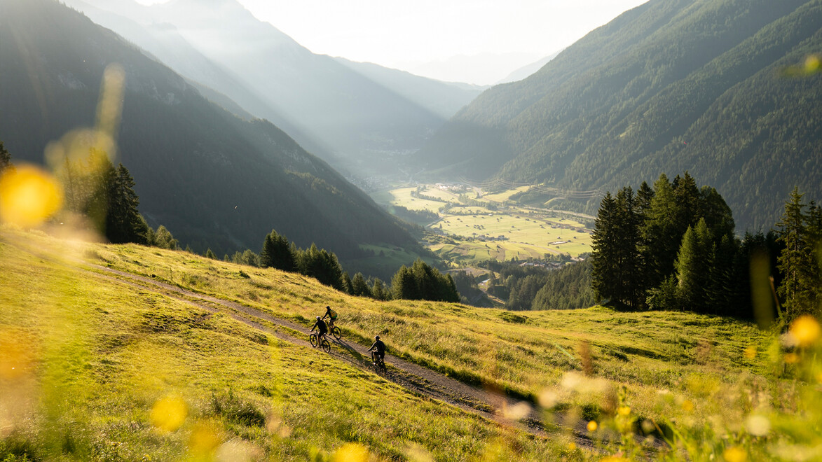 Wandernde auf einem sonnigen Hang mit Blick ins grüne Tal und umliegende Berge / Hikers on a sunny slope with views into the green valley and surrounding mountains