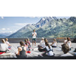 Gruppe bei Outdoor-Yoga auf einer Holzplattform vor Bergkulisse / Group during outdoor yoga on a wooden platform in front of mountain scenery