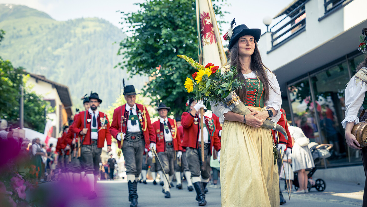 Traditioneller Festumzug mit Musikanten und Frau in Tracht mit Blumen / Traditional parade with musicians and a woman in costume holding flowers