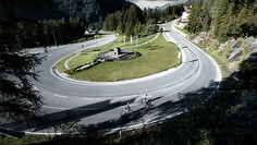 Zwei Radfahrer fahren durch eine scharfe Haarnadelkurve auf der Arlbergpassstraße, die von Wald umgeben ist.