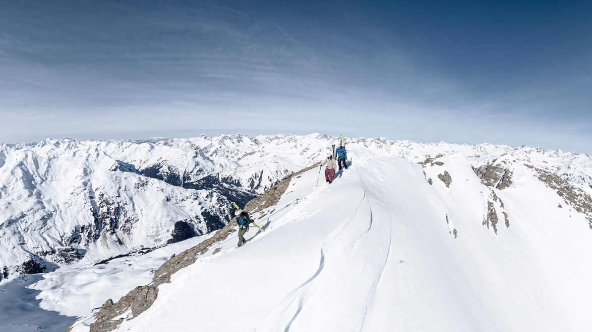 Bergsportler auf schmalem, verschneitem Grat mit weitem Panorama / Mountaineer on a narrow snowy ridge with wide mountain panorama